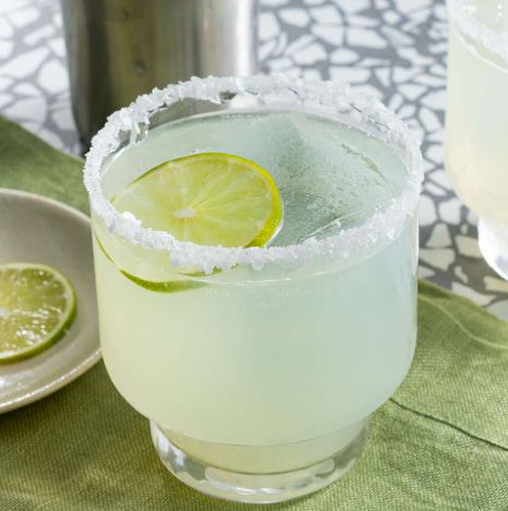 A picture of a beautiful looking margarita, in a tumbler typ class, with a slice of lime floating on the top and the rim encrusted with salt. Yummy!!